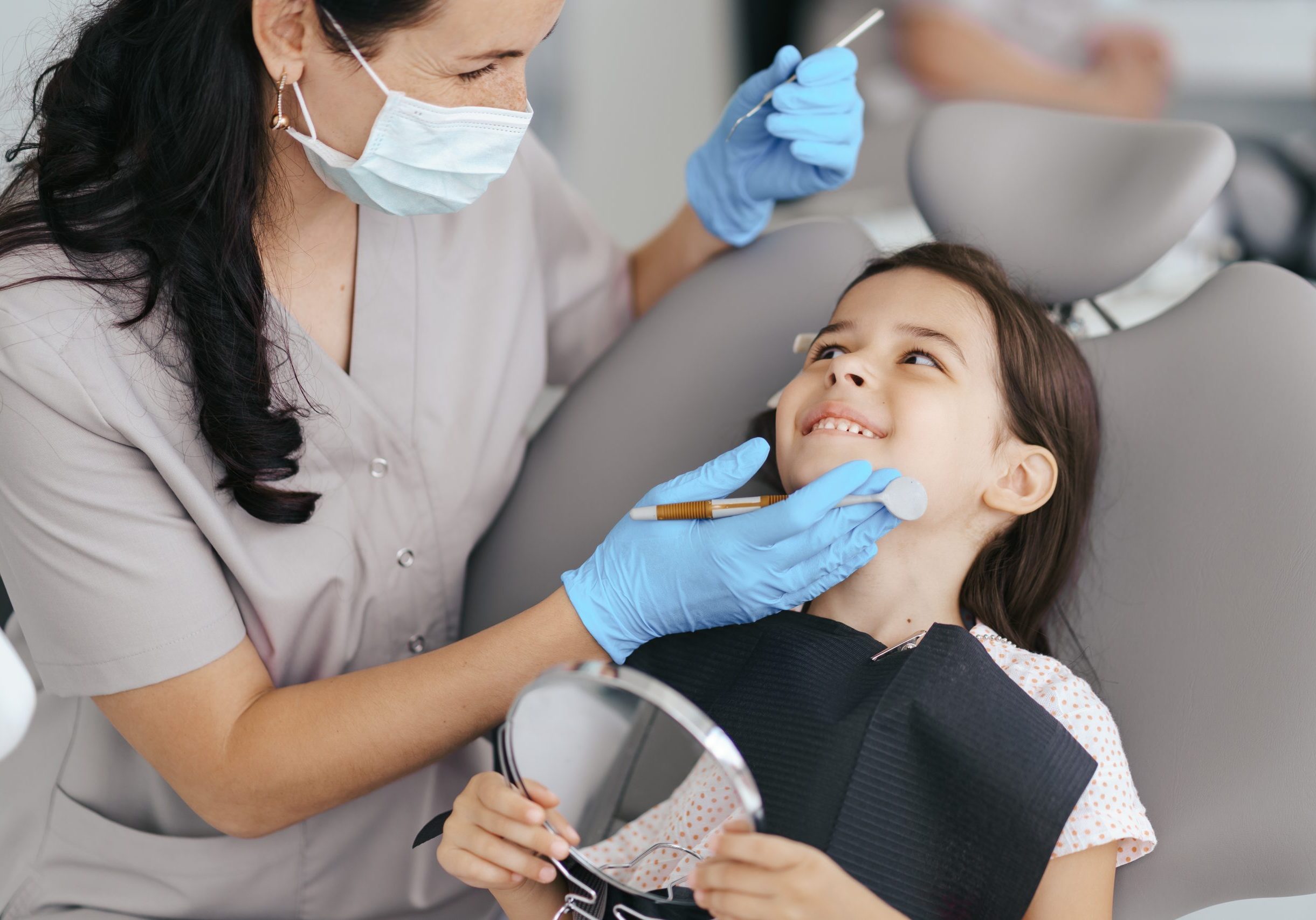 Cute little girl sitting on a modern dental chair and having dental consultation with dentist
