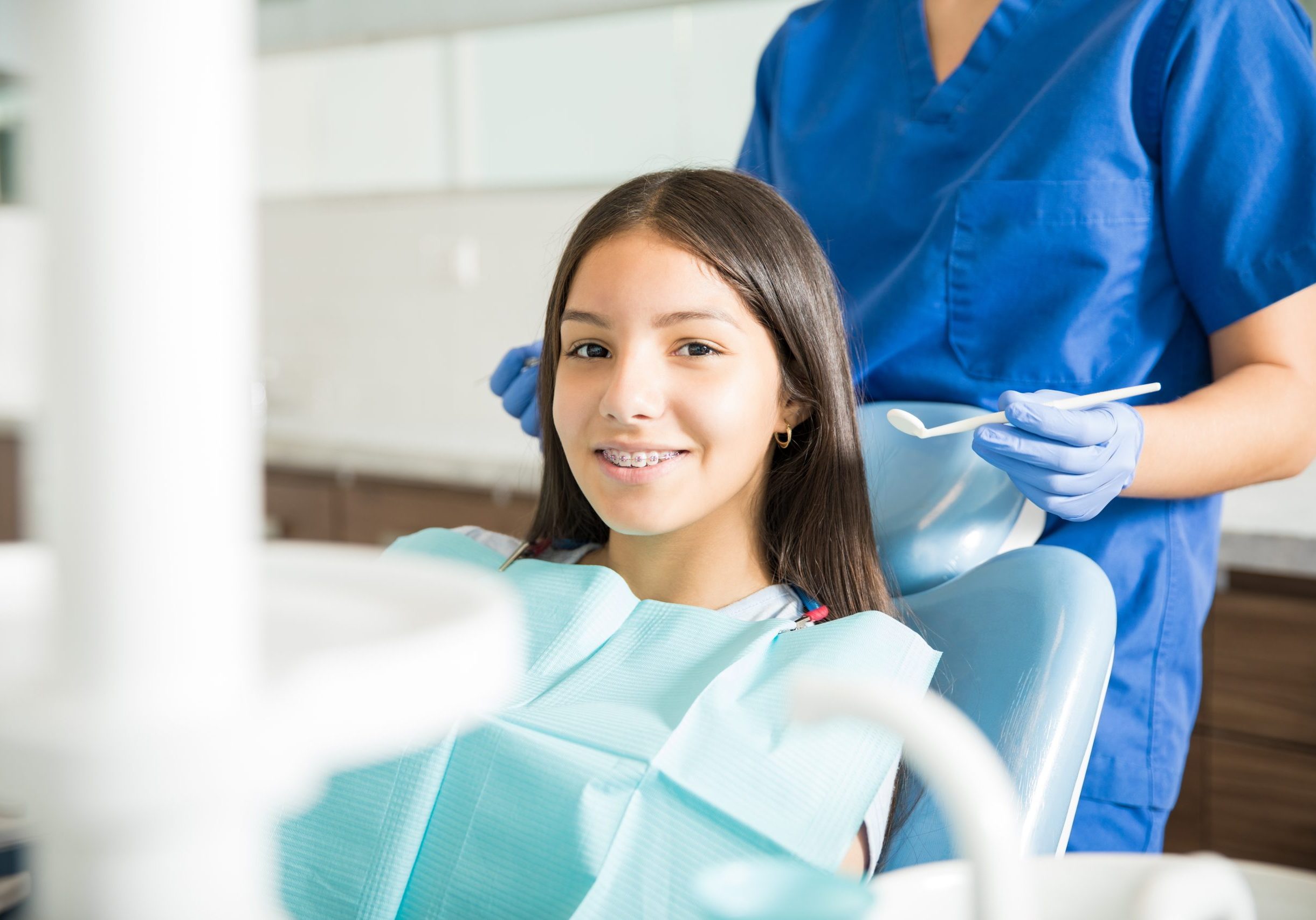 Portrait of smiling teenage girl with braces sitting on chair while dentist standing in clinic